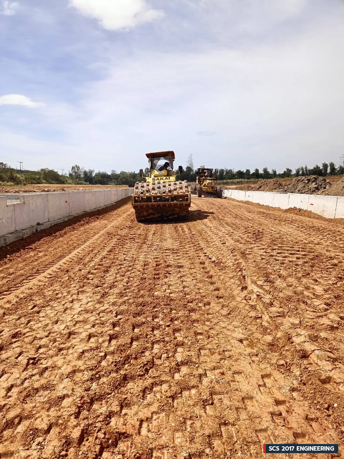 รถบดเปลือกหนาม SAKAI บดอัดชั้นดินคู่ขนานแนวกำแพงกันดินคอนกรีตเสริมเหล็ก